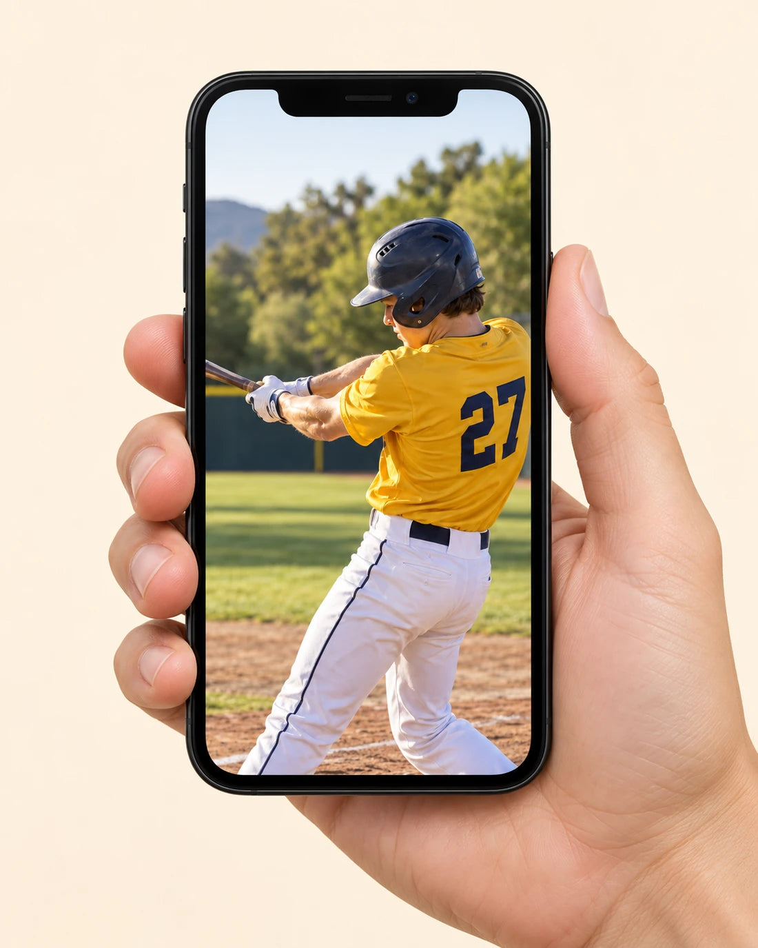 A hand holding a phone displaying a young baseball batter in a yellow jersey